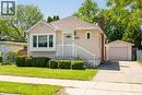 Residential exterior featuring a light-colored siding, a front entry porch with white railings, a prominent bay window, a brick chimney, and a detached garage with a driveway - 420 Upper Gage Avenue, Hamilton, ON 