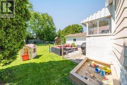 Expansive fenced backyard featuring a manicured lawn, established perimeter trees, a concrete patio area, a built-in sandbox, and a screened-in porch - 