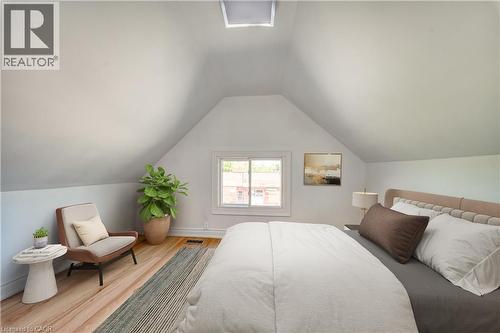 Attic bedroom featuring pitched ceilings, hardwood flooring, a single window, and a skylight Virtually stagecd - 1062 Cannon Street E, Hamilton, ON 