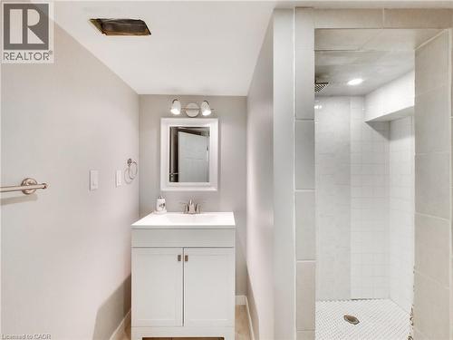Bathroom featuring a white vanity with integrated sink, chrome faucet, and rectangular mirror with task lighting - 229 Parkdale Avenue N, Hamilton, ON 