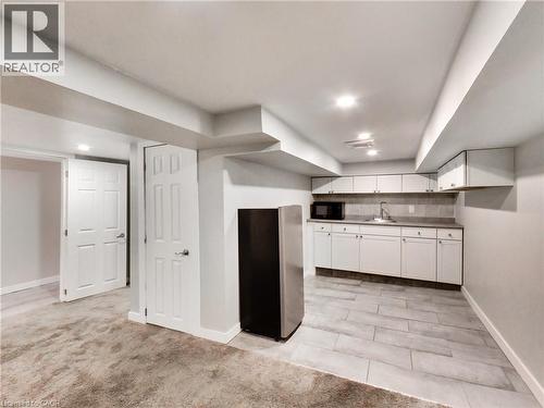 Lower-level kitchenette featuring white cabinetry, a stainless steel refrigerator, and a tile backsplash - 229 Parkdale Avenue N, Hamilton, ON 