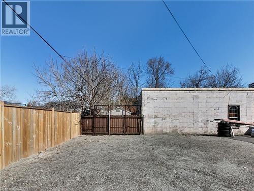 Expansive gravel lot featuring a tall wood privacy fence and a white brick structure with a single arched window - 229 Parkdale Avenue N, Hamilton, ON 