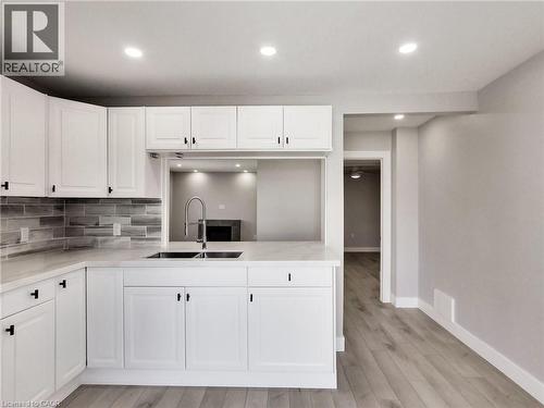 Kitchen featuring white shaker-style cabinetry, a stainless steel double basin sink with a gooseneck faucet, light-toned countertops, and a gray subway tile backsplash - 229 Parkdale Avenue N, Hamilton, ON 