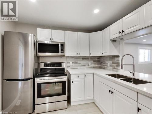 Kitchen featuring white shaker cabinetry, stainless steel appliances, light-toned countertops, a subway tile backsplash, and a double basin sink with a high-arch faucet - 229 Parkdale Avenue N, Hamilton, ON 