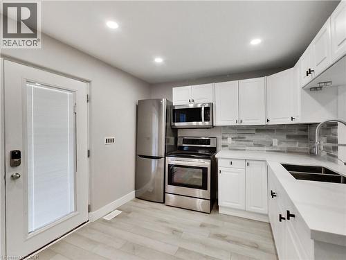 Modern kitchen featuring white shaker cabinetry, stainless steel appliances, light wood-finish flooring, a contemporary tile backsplash, and recessed lighting - 229 Parkdale Avenue N, Hamilton, ON 