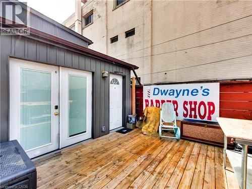 Exterior patio featuring wood decking, double glass panel doors, a single entry door with an arched transom, and gray vertical plank siding - 229 Parkdale Avenue N, Hamilton, ON 