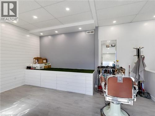 Brightly lit interior space featuring wood-finish flooring, white shiplap wall paneling, a drop ceiling with recessed lighting, and a built-in storage bench with a green surface - 229 Parkdale Avenue N, Hamilton, ON 