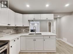 Contemporary kitchen featuring white cabinetry with black hardware, white countertops, a mosaic tile backsplash, and light wood-finish flooring - 