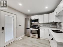 Modern kitchen featuring white shaker cabinetry, stainless steel appliances, light wood-finish flooring, a contemporary tile backsplash, and recessed lighting - 