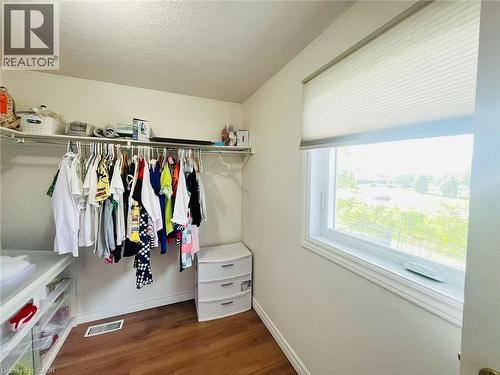 Spacious walk-in closet featuring wood-finish flooring, a single window with a privacy shade, and built-in shelving with hanging rods - 136 Hidden Creek Drive, Kitchener, ON 