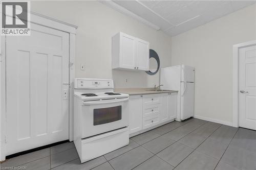 Kitchen area featuring a white electric range, white cabinetry, a single basin sink, and a white refrigerator - 1371 Main Street E, Hamilton, ON - Indoor Photo Showing Kitchen