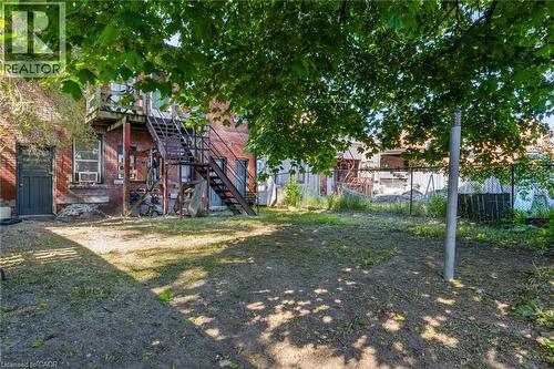 Expansive rear yard featuring mature trees, a brick facade, and a metal exterior staircase - 1371 Main Street E, Hamilton, ON - Outdoor