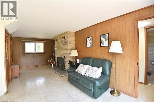 Living area featuring a stone-clad fireplace with a hearth, wood-paneled walls, and light-colored terrazzo flooring - 372 Fennell Avenue W, Hamilton, ON 
