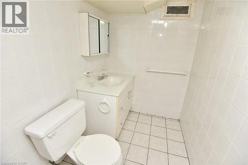 White tiled bathroom featuring a vanity with a drop-in sink, wall-mounted medicine cabinet, white toilet, and tiled flooring - 372 Fennell Avenue W, Hamilton, ON 