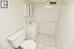 White tiled bathroom featuring a vanity with a drop-in sink, wall-mounted medicine cabinet, white toilet, and tiled flooring - 