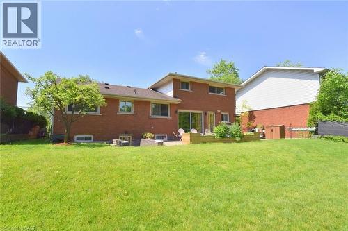Spacious rear lawn with a brick exterior, a large wooden deck, sliding glass doors, and mature landscaping - 372 Fennell Avenue W, Hamilton, ON 
