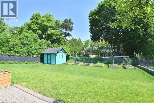Expansive green lawn featuring a turquoise shed with a dark roof, raised garden beds, a black metal fence, and mature trees - 372 Fennell Avenue W, Hamilton, ON 