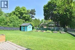 Expansive green lawn featuring a turquoise shed with a dark roof, raised garden beds, a black metal fence, and mature trees - 