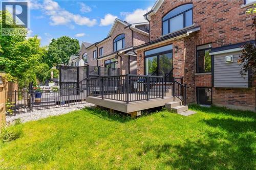 Expansive backyard featuring a lush lawn, multi-level composite decking, black metal railings, and a brick exterior with large windows and a patio door - 12 George Street, Waterloo, ON 