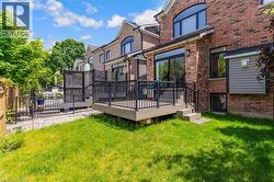 Expansive backyard featuring a lush lawn, multi-level composite decking, black metal railings, and a brick exterior with large windows and a patio door - 