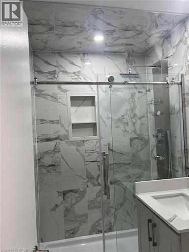 Enclosed shower with sliding glass doors, white tiled walls with grey veining, a built-in shower niche, and a rainfall showerhead - 102 Massey Avenue, Kitchener, ON 