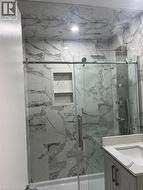 Enclosed shower with sliding glass doors, white tiled walls with grey veining, a built-in shower niche, and a rainfall showerhead - 