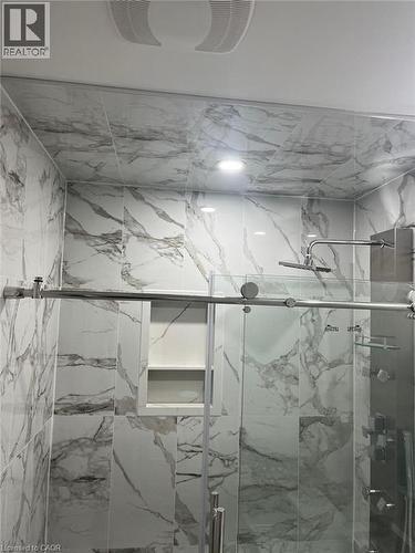 Shower enclosure featuring marble-look wall tiling, recessed lighting, a built-in shower niche, and a sliding glass door with a stainless steel bar handle - 102 Massey Avenue, Kitchener, ON 