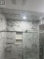 Shower enclosure featuring marble-look wall tiling, recessed lighting, a built-in shower niche, and a sliding glass door with a stainless steel bar handle - 
