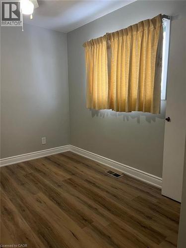 Room featuring wood-finish flooring, light grey walls, white baseboards, and a window with curtains - 102 Massey Avenue, Kitchener, ON 