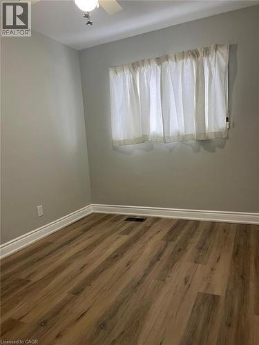 Interior space featuring wood-finish flooring, light grey walls, white baseboards, and a window with sheer white curtains - 102 Massey Avenue, Kitchener, ON 