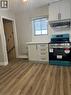 Kitchen area featuring wood-finish flooring, light-colored cabinetry with dark hardware, a freestanding range with an overhead vent, and a window with blinds - 102 Massey Avenue, Kitchener, ON 