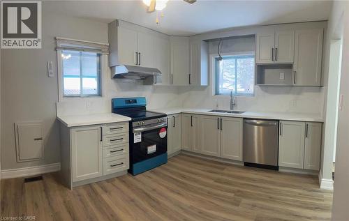 Contemporary kitchen featuring light gray shaker-style cabinetry, white countertops, stainless steel appliances, a stainless steel range hood, and wood-finish flooring - 102 Massey Avenue, Kitchener, ON 