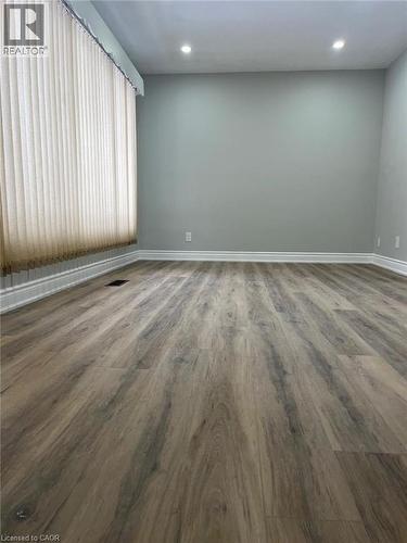 Spacious room featuring wood-finish flooring, light gray wall paint, and recessed ceiling lighting - 102 Massey Avenue, Kitchener, ON 