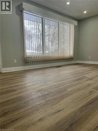 Wood-finish flooring throughout, featuring a large window with vertical blinds, recessed lighting, and crisp white baseboards - 102 Massey Avenue, Kitchener, ON 