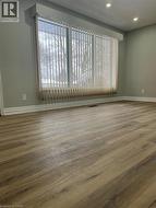 Wood-finish flooring throughout, featuring a large window with vertical blinds, recessed lighting, and crisp white baseboards - 