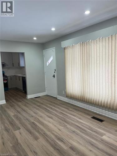 Spacious room featuring wood-finish flooring, recessed ceiling lighting, a white entry door, and a large window with vertical blinds - 102 Massey Avenue, Kitchener, ON 