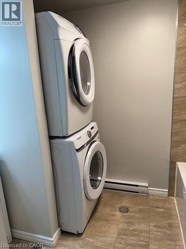 Dedicated laundry area featuring a stacked washer and dryer, tile flooring, and a baseboard heater - 113 Cornerbrook Crescent Unit# 2, Waterloo, ON 