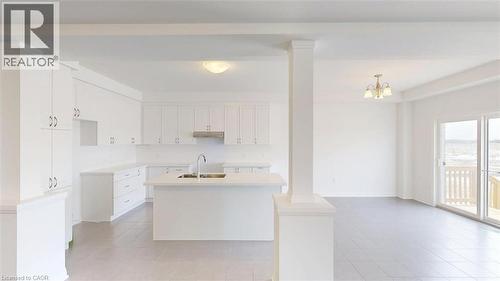 Open-concept kitchen and living area featuring white cabinetry, a center island with a sink, stainless steel range hood, and light-toned tile flooring - 287 Rockledge Drive, Hamilton, ON 
