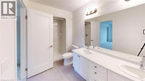 Bathroom featuring a double vanity with two undermount sinks, a long wall-mounted mirror, brushed nickel light fixtures, a toilet, and a stand-up shower with a single-handle faucet - 287 Rockledge Drive, Hamilton, ON 