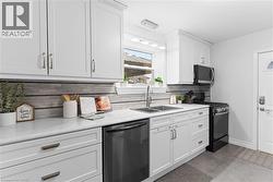 Modern kitchen featuring white shaker cabinetry, light-toned countertops, a stainless steel double sink with a gooseneck faucet, a grey horizontally-stacked tile backsplash, and a black appliance suit - 