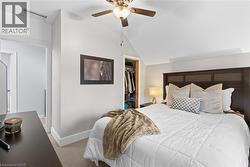 Bedroom featuring a wood-panel headboard, textured carpeting, ceiling fan with light fixture, and an open closet with built-in shelving - 