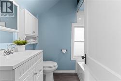 Bathroom featuring a white vanity with integrated sink, chrome faucet, white wall-mounted cabinet, toilet, and a window with white trim - 
