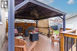Spacious wood-finish deck featuring a permanent gazebo structure, decorative privacy screens, perimeter railing, and integrated wall lighting - 