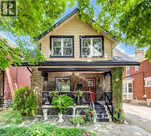 Brick exterior with a covered front porch featuring black railings and a red entry door - 78 Chestnut Street, Kitchener, ON 