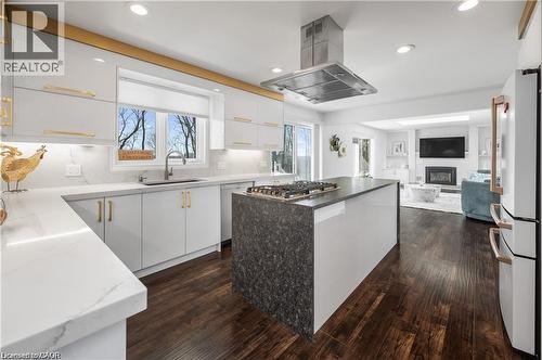 Modern kitchen featuring a gas cooktop on a central island with a stone-finish side panel, under-cabinet lighting, a stainless steel range hood, and wood-finish flooring - 355 Edgehill Drive, Kitchener, ON 