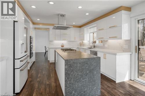 Gourmet kitchen featuring a large waterfall island with integrated cooktop, white cabinetry with gold-tone hardware, wood-finish flooring, recessed lighting, and a sliding glass door to exterior - 355 Edgehill Drive, Kitchener, ON 