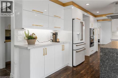 Modern kitchen featuring white cabinetry with gold-tone hardware, white quartz countertops, under-cabinet lighting, a built-in refrigerator, and wood-finish flooring - 355 Edgehill Drive, Kitchener, ON 