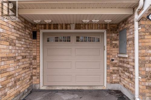 Brick exterior featuring a paneled garage door with upper window inserts, an overhead soffit, and exterior lighting fixtures - 7 Sirente Drive Unit# 11, Hamilton, ON - Outdoor With Exterior