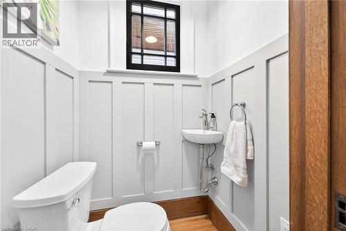 Powder room featuring a wall-mounted sink with chrome fixtures, a white toilet, and board and batten paneling - 22 Connaught Avenue S, Hamilton, ON 
