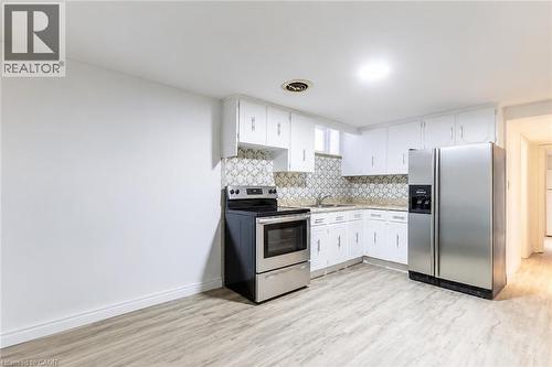 Kitchen featuring white cabinetry, stainless steel appliances, patterned tile backsplash, and light wood-finish flooring - 404 Queenston Road, Hamilton, ON 
